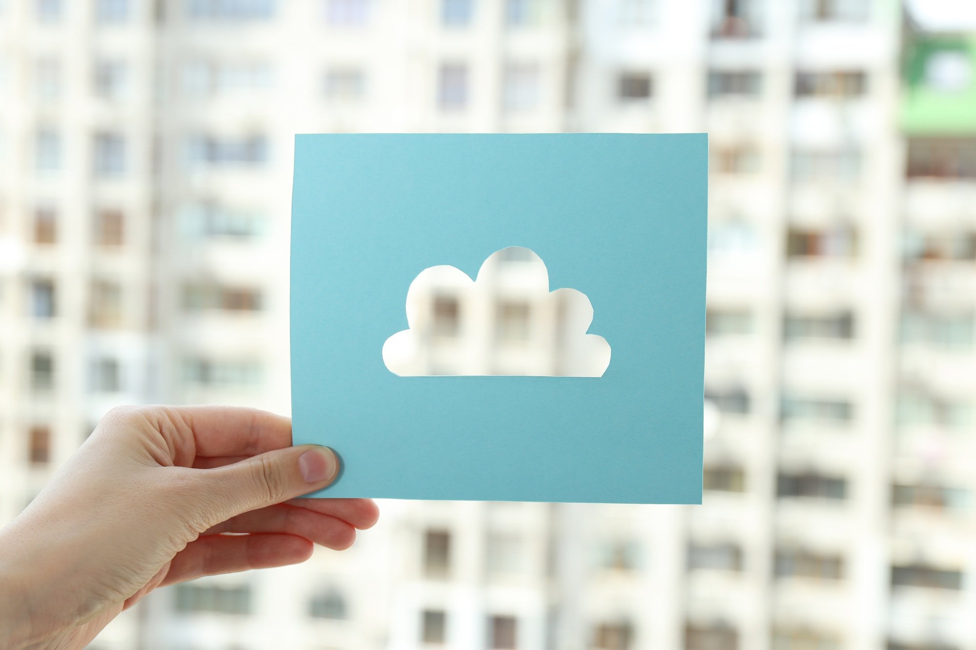 The cloud is cut out of paper in the hand against the background of the city