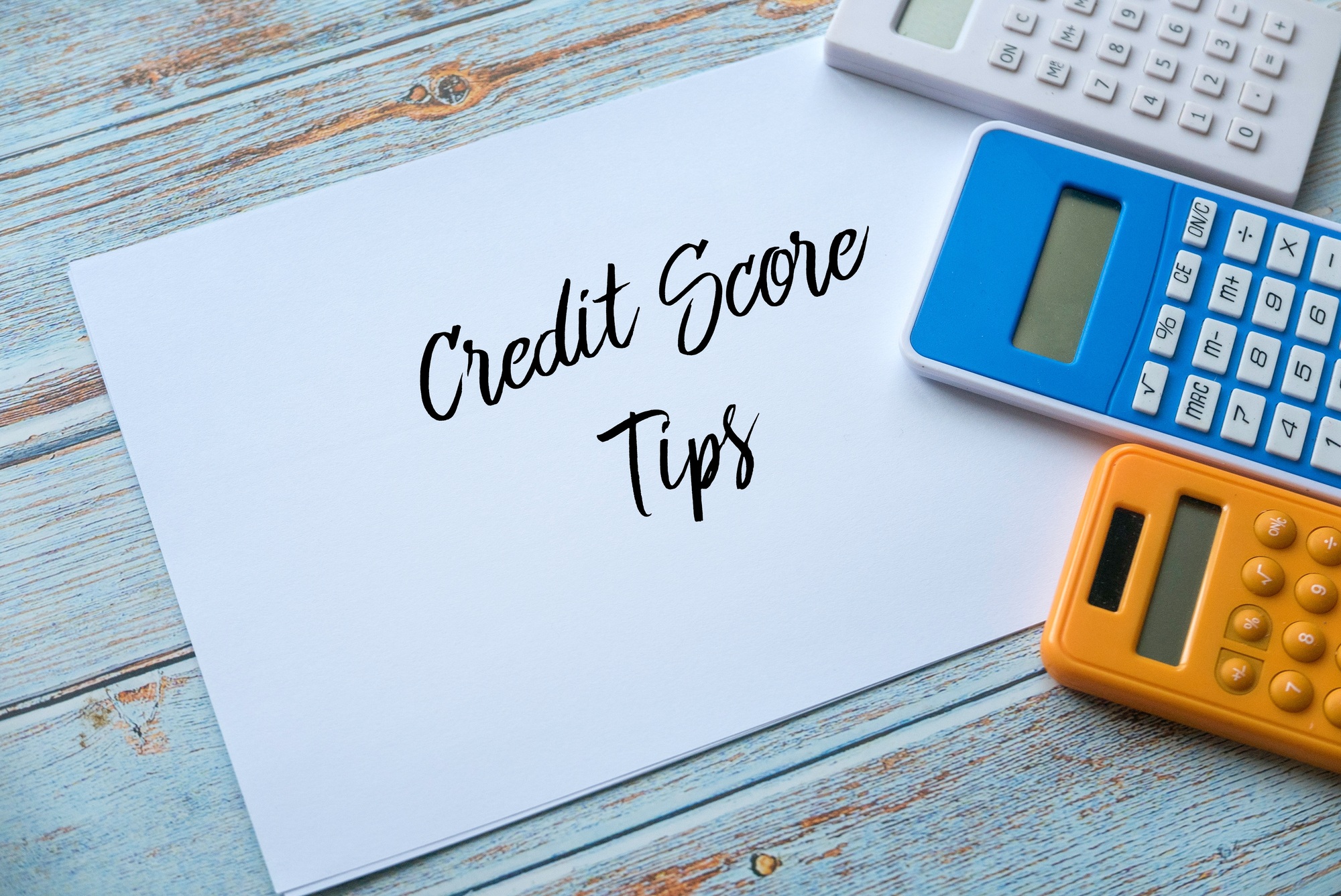 Top view of calculator and paper written with Credit Score Tips on wooden background.