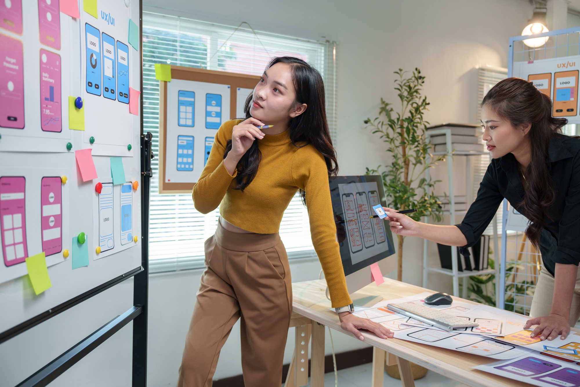 Two female web designers are discussing ux and ui design for mobile application development, working