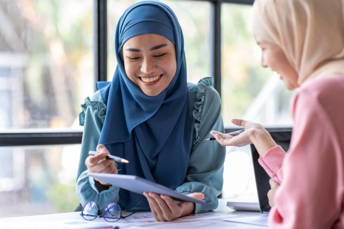 Two Young muslim business women point to graphs and charts to analyze market data, balance sheet, ac