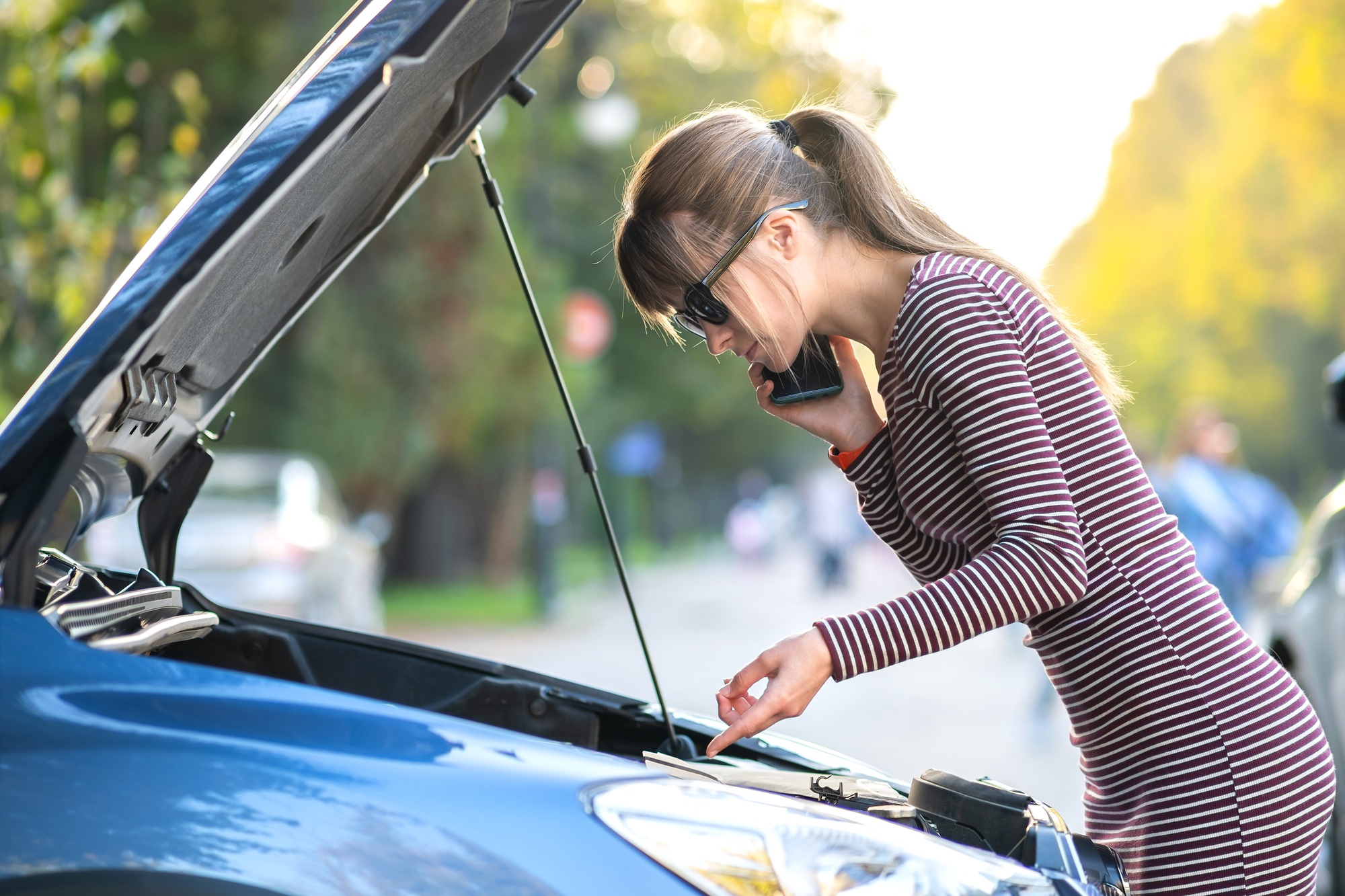 Upset young woman driver talking angrily on cell phone with assistance service