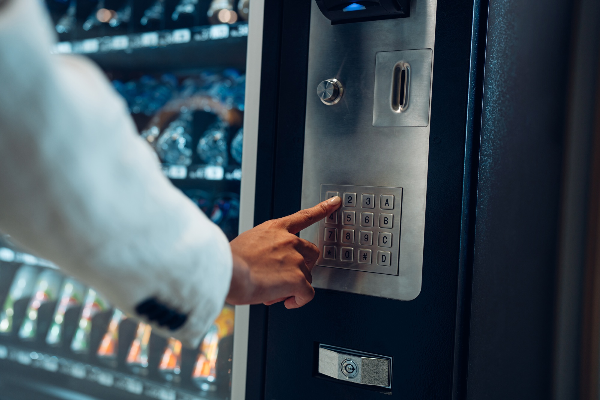 woman's finger pushing number button on keyboard of snack vending machine.