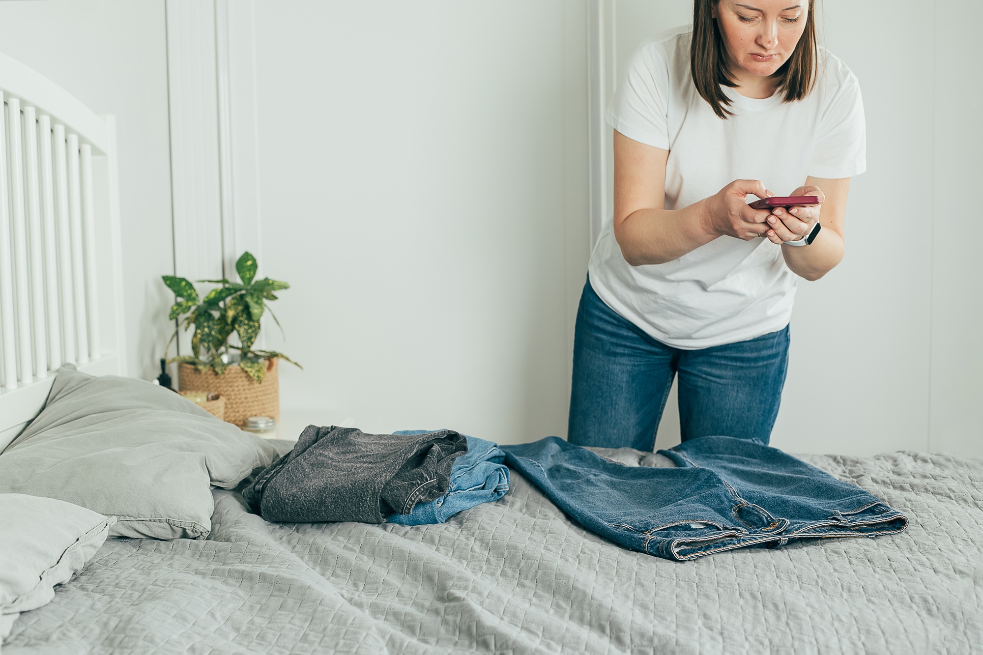 Woman taking photo of jeans on smartphone. Concept of secondhand, online sale, sustainability
