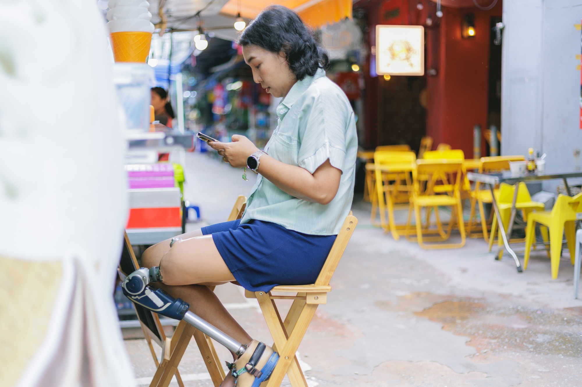 Woman with Prosthetic Leg Using Phone While Preparing Food Truck in a Casual Street Setting