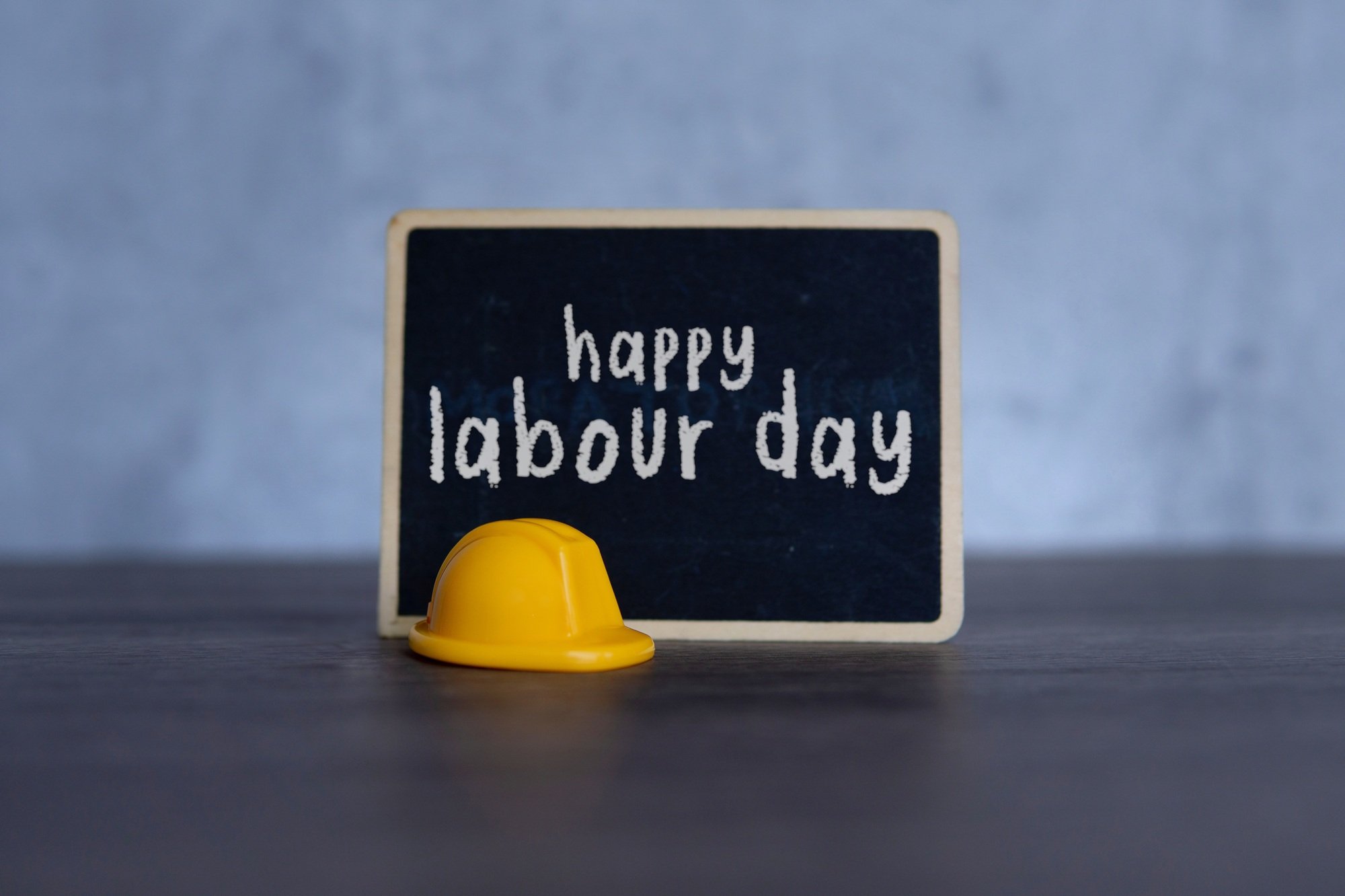 Yellow hard hat and chalkboard with text HAPPY LABOUR DAY.