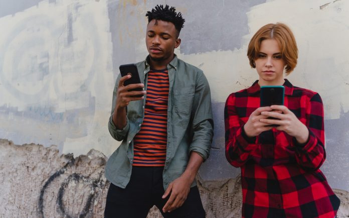 Young biracial couple addicted to smartphones outdoors in town, social media concept