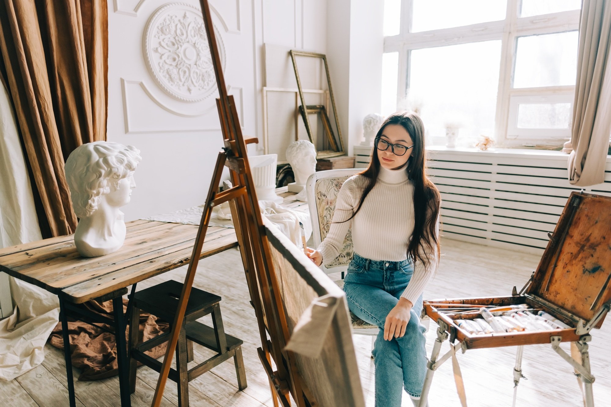 Young caucasian woman artist, holding paintbrush and draws on canvas , working on a home studio.
