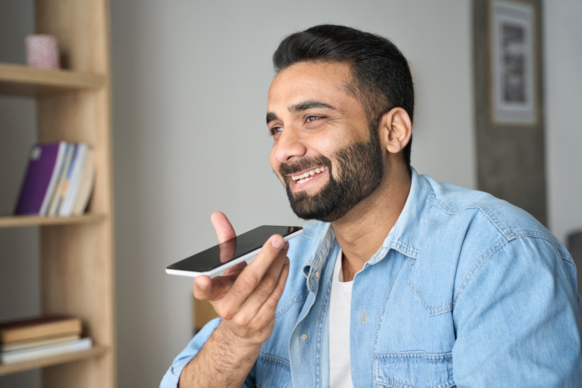 Young indian man speaking to voice assistant using smartphone.