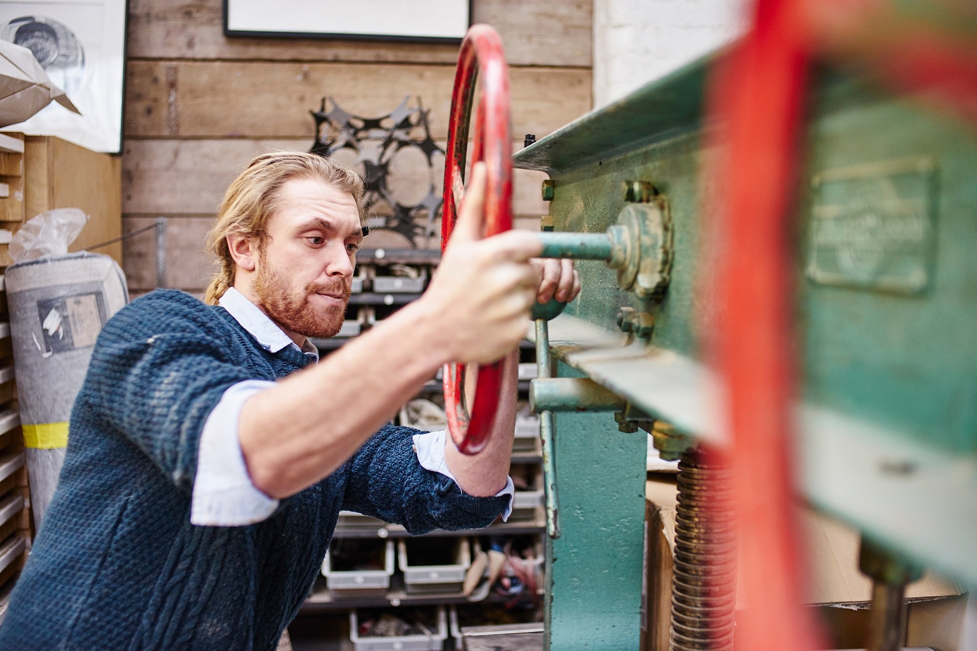Young man turning print press wheels in traditional print workshop