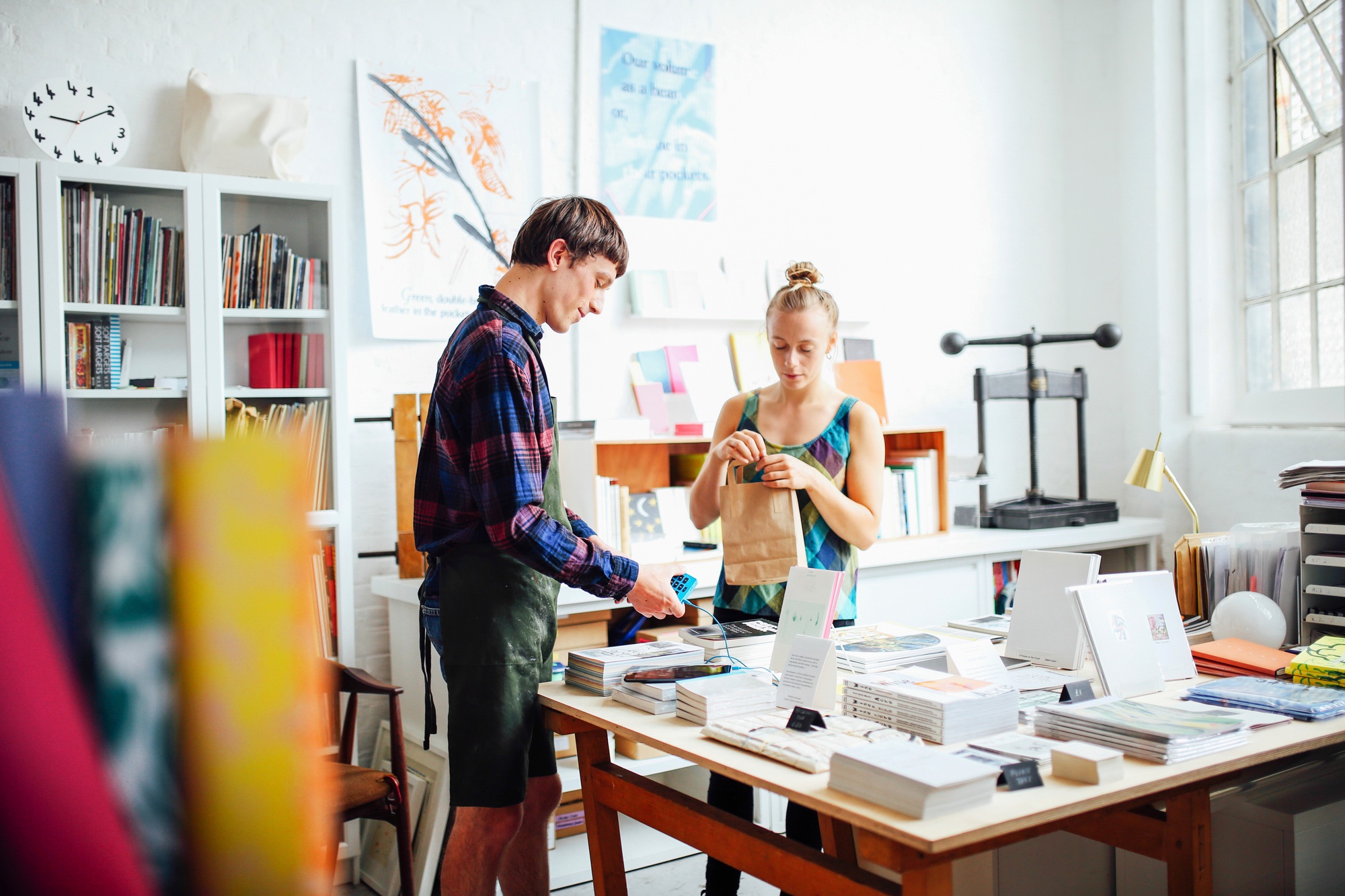 Young woman buying book from young craftsman in art bookshop